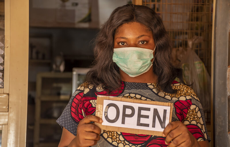 Local african business owner holding a open sign in her store